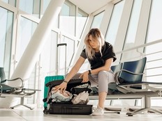 Serious woman with luggage sitting in waiting room at the international airport, packing suitcase with clothes