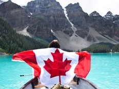 Young girl in a canoe holding canadian flag, in front of turquoise Lake Moraine and mountains