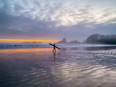 A surfer walking at sunset on Long Beach in Tofino, B.C.