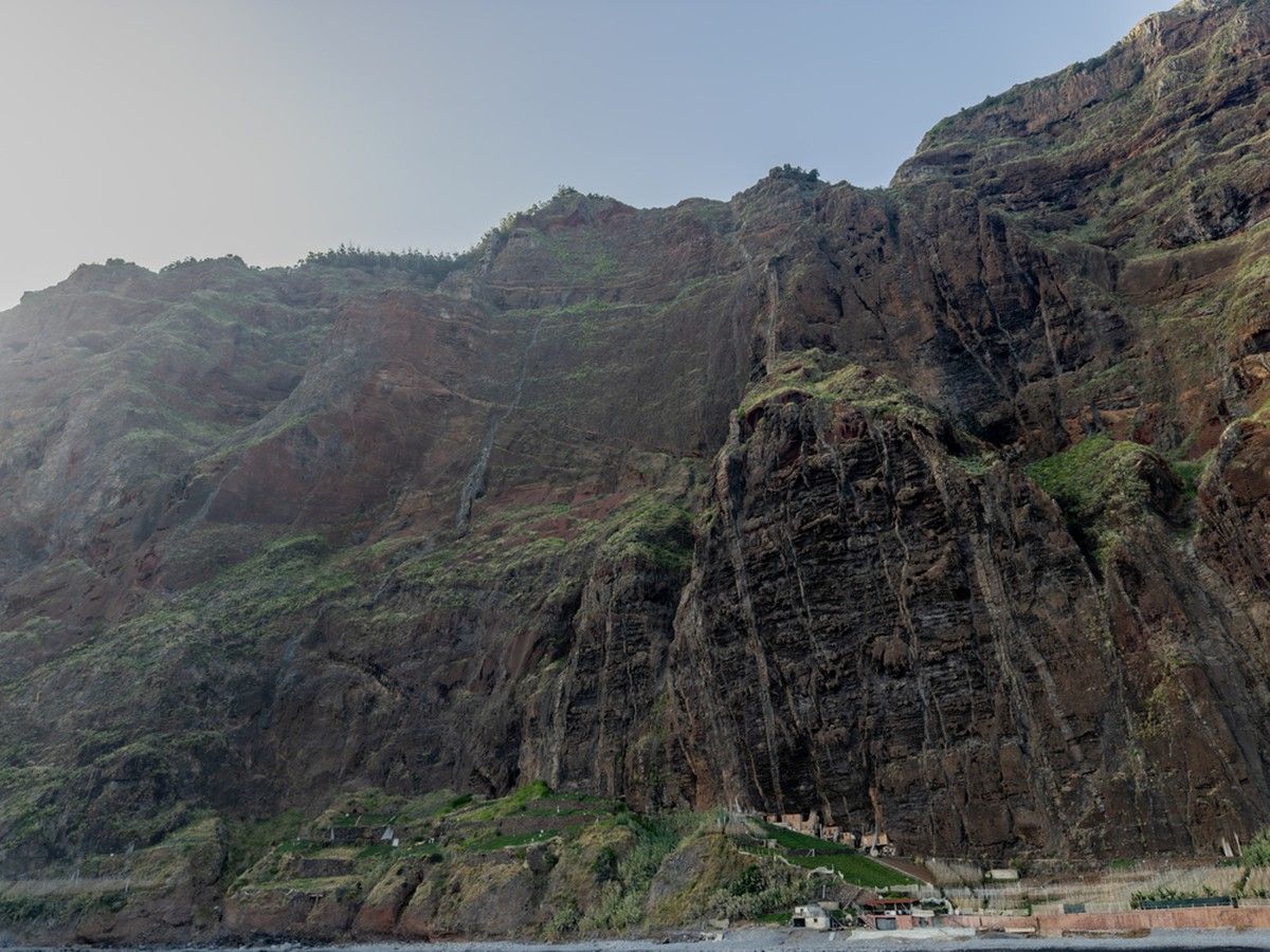 Viewed from sea level, the sheer rock face of Cabo Girão rises above small coastal agricultural terraces.