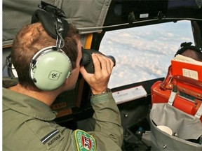 In this March 22, 2014 file photo, an officer onboard a Royal Australian Air Force P-3 Orion uses binoculars during the search for missing Malaysian Airlines flight MH370 in southern Indian Ocean, Australia. (AP Photo/Rob Griffith, File)