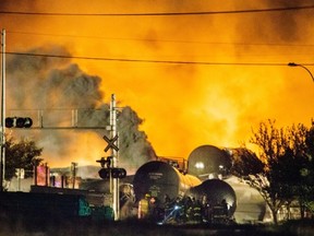 Smoke and fire rises over train cars as firefighters inspect the area after a train carrying crude oil derailed and exploded in the town of Lac-Megantic, 100 kilometres east of Sherbrooke on Saturday, July 6, 2013.