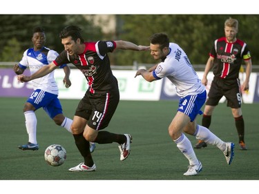 Ottawa Fury midfielder Tony Donatelli (centre) battles for the ball against Edmonton FC's Ritchie Jones (right) during the teams match-up at Keith Harris Stadium in Ottawa, May 31, 2014.
