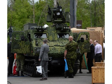 People make their way past a display of an armoured vehicle at the CANSEC trade show in Ottawa on Wednesday, May 28, 2014. The bombs and mortars on display are models.