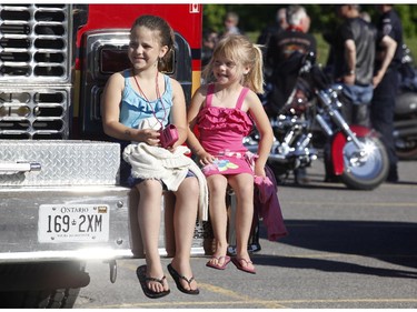 Victoria (L), 9, and Isabelle, 7, sit on the bumper of a fire truck as they watch the Ottawa TELUS Motorcycle Ride for Dad at the Canadian Aviation and Space Museum on Saturday May 31, 2014.