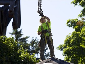 A worker on the rooftop guides lifting chains as they prepare to remove the roof of a house on Rodney Crescent. The house is being removed from its current location. (Pat McGrath / OTTAWA CITIZEN)