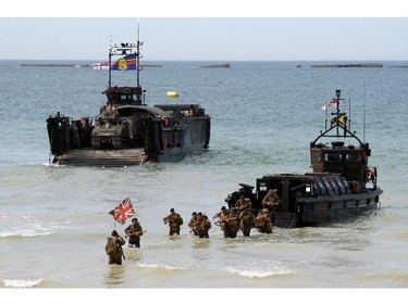 A group of military re-enactors feign a landing of a World War II barge on the beach  of Arromanches, France,  Friday, June 6, 2014, as part of D-Day commemorations. World leaders and veterans gathered by the beaches of Normandy on Friday to mark the 70th anniversary of World War Two's D-Day landings.