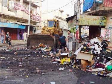 A municipality bulldozer and people clean up trash from a street in the northern city of Mosul, Iraq, Friday, June 13, 2014. Iraqi officials say al-Qaida-inspired militants who this week seized much of the country's Sunni heartland have pushed into an ethnically mixed province northeast of Baghdad, capturing two towns there.(AP Photo)
