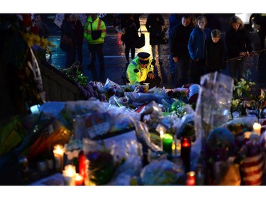 A RCMP officer places a candle as people take part in a candlelight vigil outside RCMP headquarters in Moncton, N.B., on Friday, June 6, 2014. RCMP say a man suspected in the shooting deaths of three Mounties and the wounding of two others in Moncton was unarmed at the time of his arrest early Friday and was taken into custody without incident.