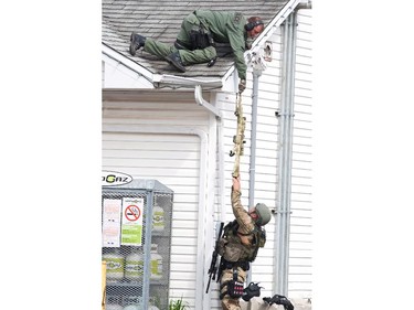 A weapon is passed to an Emergency Response Team member on the roof of a house in Moncton, N.B., Thursday, June 5, 2014 as the search for a heavily armed gunman suspected to have shot three Mounties dead and injured two others continues.