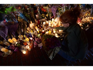 A woman lights a candle during a candlelight vigil outside RCMP headquarters in Moncton, N.B., on Friday, June 6, 2014. RCMP say a man suspected in the shooting deaths of three Mounties and the wounding of two others in Moncton was unarmed at the time of his arrest early Friday and was taken into custody without incident.