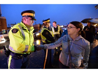 A woman shakes hands with a RCMP officer at a candlelight vigil outside RCMP headquarters in Moncton, N.B., on Friday, June 6, 2014. RCMP say a man suspected in the shooting deaths of three Mounties and the wounding of two others in Moncton was unarmed at the time of his arrest early Friday and was taken into custody without incident.