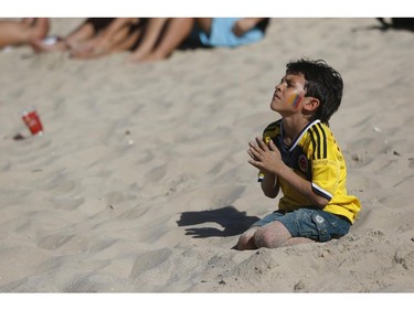A young Colombia soccer fan kneels with his hands clasped as he watches his team's World Cup game against Greece inside the FIFA Fan Fest area on Copacabana beach in Rio de Janeiro, Brazil, Saturday, June 14, 2014.