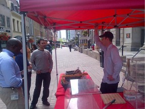 Art Is In Bakery stand at the Sparks Street Market. It is all the remains of a market where nine other vendors used to stretch along the pavement that is now empty in the background. The vendor behind the stand is Ty Simpson.