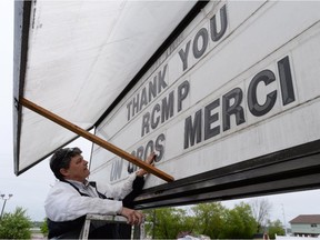 Elaine Mason puts up a sign outside the Rodd Moncton Hotel in Moncton, N.B., on Friday, June 6 . RCMP say a man suspected in the shooting deaths of three Mounties and the wounding of two others in Moncton was unarmed at the time of his arrest early Friday and was taken into custody without incident.