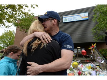 Jeff Pyke is comforted after placing flowers for friend Const. Douglas Larche outside RCMP headquarters in Moncton, N.B., on Friday, June 6, 2014. RCMP say a man suspected in the shooting deaths of three Mounties and the wounding of two others in Moncton was unarmed at the time of his arrest early Friday and was taken into custody without incident.