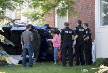 Urbandale superintendent Dale Rief, left, and property manager Margaret Campbell speak with Ottawa police officers as they take in the damage to a vehicle with its roof removed lays on its side after it crashed into a house on Steeplechase Drive in Kanata on Sunday, June 15, 2014.