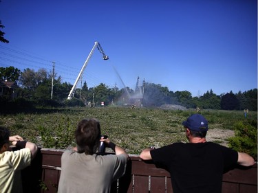 Nearby residents watch firefighters extinguish a blaze in an uninhabited building early Saturday morning on Presland Road near the Vanier Parkway on June 7, 2014.