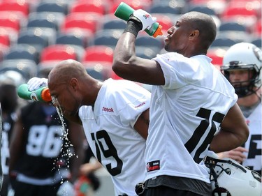 Paris Jackson #19 (L) and Marcus Henry #16 (R) of the Ottawa Redblacks cool off from the heat with water during a practice at TD Place stadium in Ottawa on June 29, 2014.