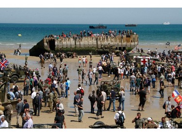 People throng the beach of Arromanches, France, as World War II vehicles are displayed, Friday, June 6, 2014, as part of D-Day commemorations.  World leaders and veterans gathered by the beaches of Normandy, northern France, on Friday to mark the 70th anniversary of the World War II D-Day landings.