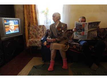 Vera Yunets (L), a pro-Russian supporter aged 83, wearing military decorations, watches a TV broadcast of the inauguration of Ukrainian President Petro Poroshenko as her son Valeriy reads the paper, on June 7, 2014, at her home in the small eastern Ukrainian town of Ilovaisk, in the Donetsk region.
