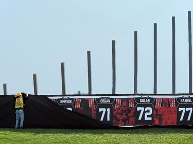 A construction worker hurries to cover up the retired jerseys of legendary Ottawa football players - which will be unveiled at the Redblack's home opener tonight - after its cover blew off.  On the inaugural opening day of TD Place July 18, 2014.