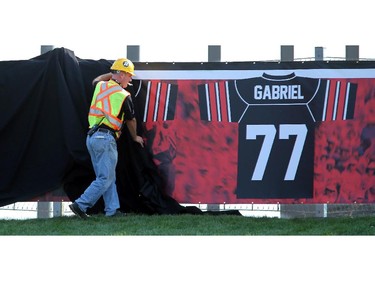 A construction worker hurries to cover up the retired jerseys of legendary Ottawa football players - which will be unveiled at the Redblack's home opener tonight - after its cover blew off. On the inaugural opening day of TD Place July 18, 2014.
