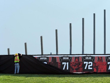 A construction worker hurries to cover up the retired jerseys of legendary Ottawa football players - which will be unveiled at the Redblack's home opener tonight - after its cover blew off.  On the inaugural opening day of TD Place July 18, 2014.