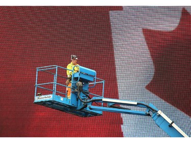 A construction worker squeezes in a short smoke break while hoisted high into the air on a crane in front of the new TD Place jumbo screen overlooking the field as the Ottawa Redblacks practice through a downpour Tuesday morning at TD Place Stadium at Lansdowne Park.