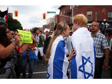 A couple wearing Israeli flags pass by as people march with the Palestinian Flag and signs on Saturday, July 26, 2014 as they call for an end to the war in Gaza.