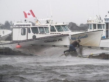 A lobster fisherman slips but holds on while trying to secure lines to his fishing boat after the floating dock broke apart during Tropical storm Arthur in Escuminac, N.B. on Saturday, July 5, 2014.