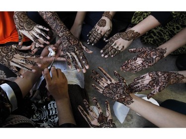 A Pakistani beautician paints the hands of customers with henna ahead of the Muslim Eid al-Fitr holiday, ending the fasting month of Ramadan, in Karachi, Pakistan, on Sunday, July 27, 2014.