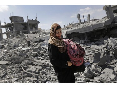 A Palestinian woman carries her belongings past the rubble of houses destroyed by Israeli strikes in Beit Hanoun, northern Gaza Strip, Saturday, July 26, 2014. Thousands of Gaza residents who had fled Israel-Hamas fighting streamed back to devastated border areas during a lull Saturday, and were met by large-scale destruction: scores of homes were pulverized, wreckage blocked roads and power cables dangled in the streets.