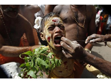 A young Indian Hindu devotee reacts in pain as he gets his cheeks pierced with a steel rod as part of a ritual during �Aadi� celebrations in Chennai, India, Sunday, July 27, 2014. Aadi, a holy month for Tamils is celebrated with rituals worshipping Hindu goddess Durga.