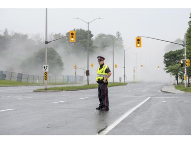 An Ottawa Police officer blocks Carling Avenue as smoke fills the air following the demolition of the Sir John Carling building in Ottawa on Sunday, July 13, 2014. The former headquarters of Agriculture and Agri-Food Canada at 930 Carling, completed in 1967, is being demolished at a cost of $4.8 million.