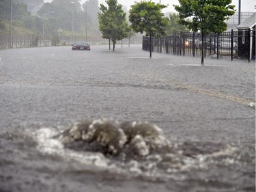 As a water drain overflows a vehicle sits in the flooded waters on Friday, July 4, 2014, in New Bedford, Mass., after heavy rains from Hurricane Arthur.