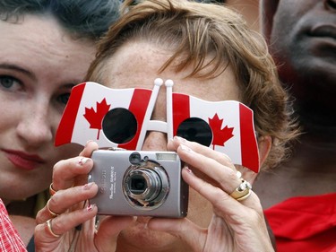 A woman wearing Canadian flag-shaped sunglasses takes a photo while taking part in celebrations on Parliament Hill in Ottawa, Tuesday, July 1, 2014.