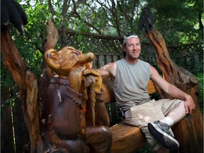 Chainsaw Sculpture artist Josh Dagg sits with a bench culpture he made in an Almyer garden.