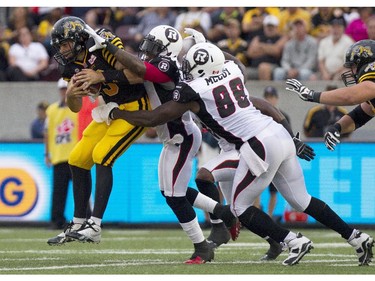 Hamilton Tiger-Cats quarterback Dan LeFevour, left, is tackled by Ottawa RedBlacks Jovon Johnson, centre, and Chris McCoy during their CFL home opener in Hamilton, Ont., Saturday, July 26, 2014.