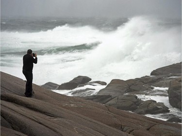 Photographer Gary Brinton braves the elements on the rocks at Peggy's Cove, N.S. as residents begin to feel the effects of tropical storm Arthur on Saturday, July 5, 2014. Thousands of homes and businesses were without power as heavy rains and high winds buffeted the region.