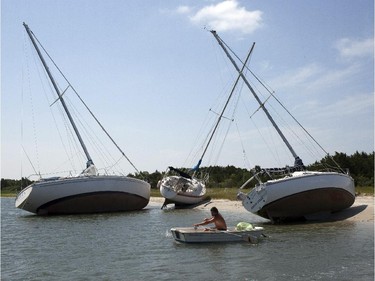 Jim Bonavito, of Beaufort, N.C., rows his dingy, Friday, July 4, 2014, past sailboats that broke free of their moorings during the winds and waves from Hurricane Arthur in Beaufort. Arthur began moving offshore and away from the southern state early Friday.