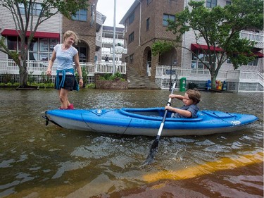 Lauren Heesemann, left, smiles at her nephew Summit Gibson, 7, from Oklahoma as he tries to maintain his balance on the kayak through a flooded street on Friday, July 4, 2014, in Manteo, N.C. The storm was expected to bring a lousy July Fourth beach day with it as it moved offshore of the northeast coast.