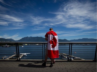 A man wearing a Canadian flag on his back takes in the view of the harbour and north shore mountains during Canada Day celebrations in Vancouver, B.C., on Tuesday July 1, 2014.
