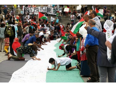 People march sign the Palestinian Flag as it lays on Parliament Hill on Saturday, July 26, 2014 as they call for an end to the war in Gaza.