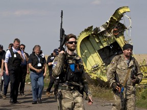 Pro-Russian rebels, right, followed by members of the OSCE mission, walk by plane wreckage as they arrive for a media briefing at the crash site of Malaysia Airlines Flight 17, near the village of Hrabove, eastern Ukraine, Tuesday, July 22, 2014. A team of Malaysian investigators visited the site along with members of the OSCE mission for the first time since last week's crash.