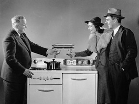 An appliance salesman stands behind a stove, showing a stopwatch to a husband and wife as they watch a pot on the burner, 1940s. The women wears a fur-collared coat. [circa 1945] Credit: Hulton|Archive by Getty Images