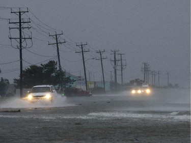 Vehicles navigate a flooded Highway 64 as wind pushes water over the road as Hurricane Arthur passes through Nags Head, N.C., Friday, July 4, 2014.