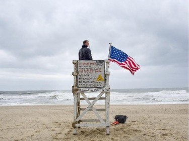 While strong, gusty winds arrive at the Oceanfront Virginia Beach Lifeguard David Derrick tends to his duties on Friday, July 4, 2014, in Virginia Beach, Va. The storm was expected to bring a lousy July Fourth beach day with it as it moved offshore of the northeast coast.