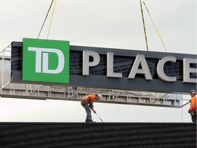 Workers carefully lower the TD PLACE sign into place atop the massive scoreboard.