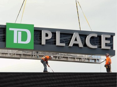 Workers carefully lower the TD Place sign into place atop the massive scoreboard as the Ottawa Redblacks practice at TD Place Stadium at Lansdowne Park on Monday, July 14, 2014.